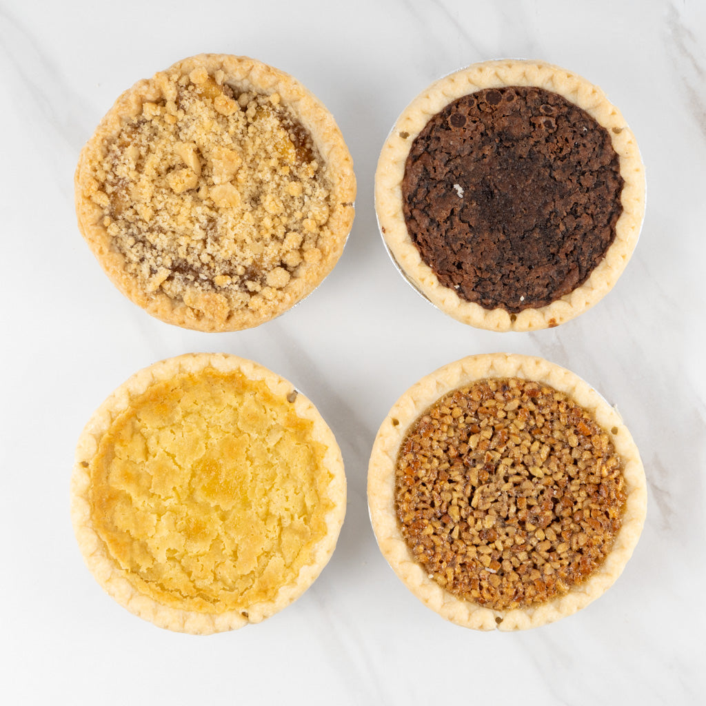 Four 4" pies arranged in a square. Tangy Buttermilk, toasty Pecan, sweet Apple Crumb, and rich Heavenly Chocolate.