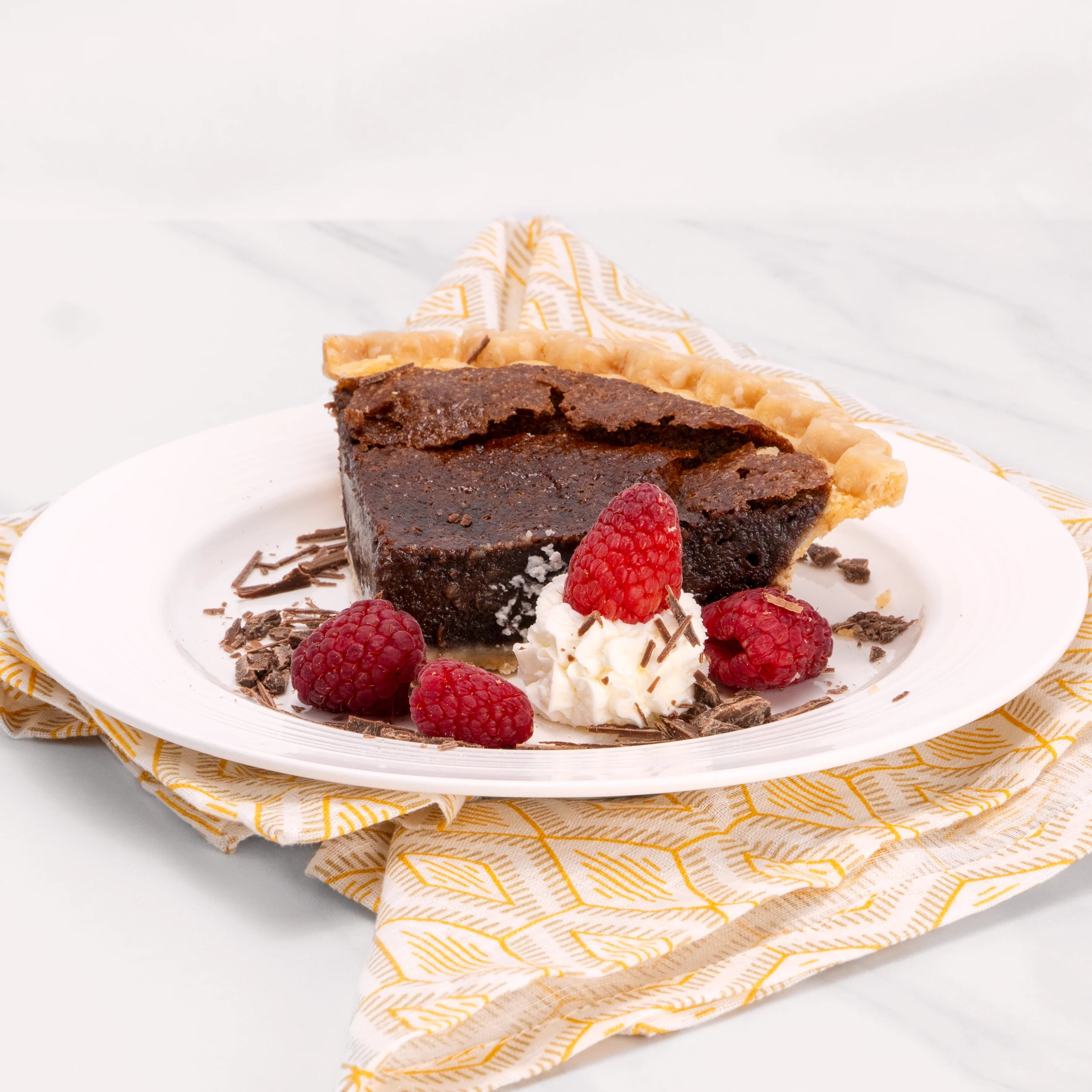 Slice of Gluten Free Chocolate Midnight Marquise cake garnished with chocolate, raspberries, and a dollop of crème.