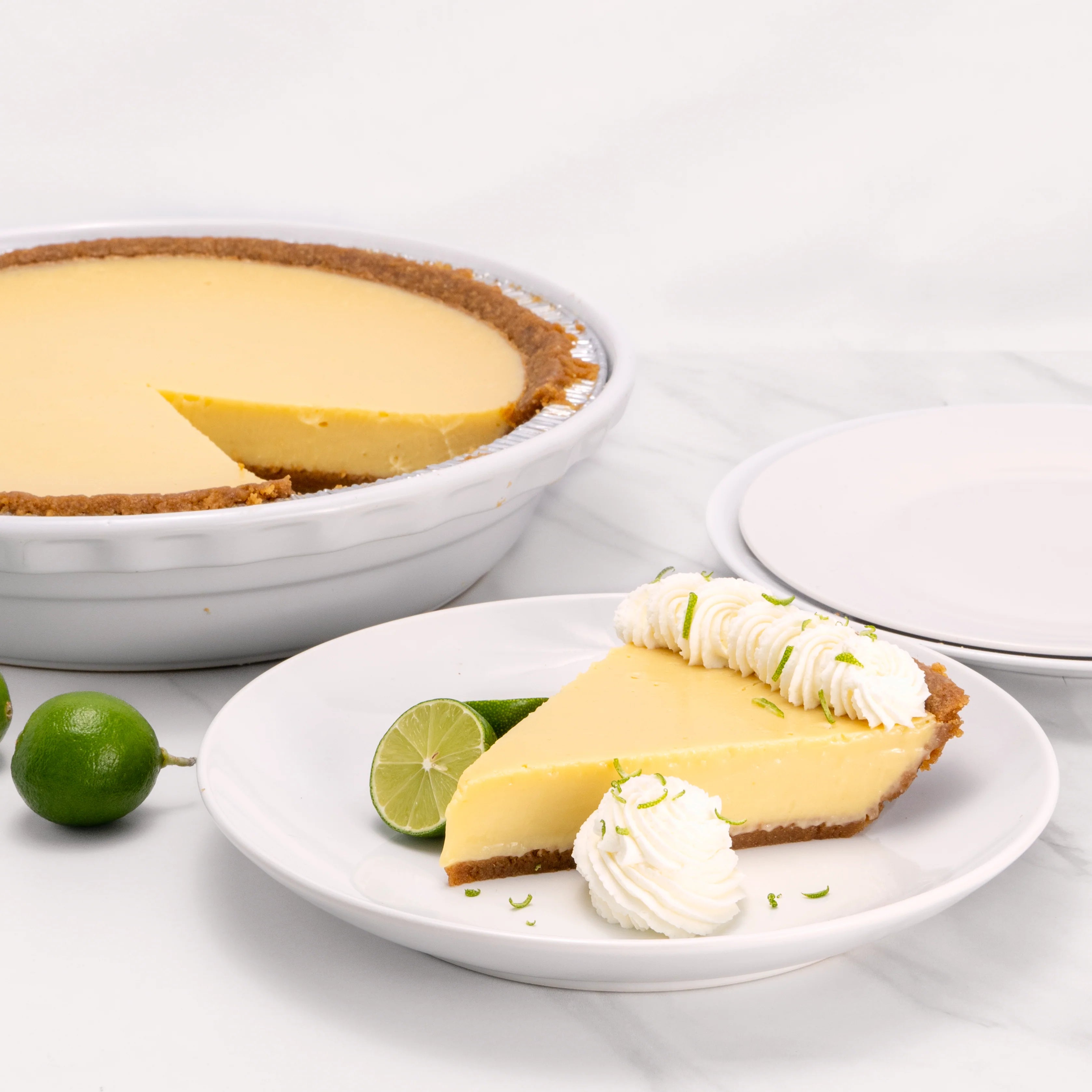 Slice of Key Lime Pie, garnished with lime and a dollop of crème, in front of an 9" cake from which it was cut.