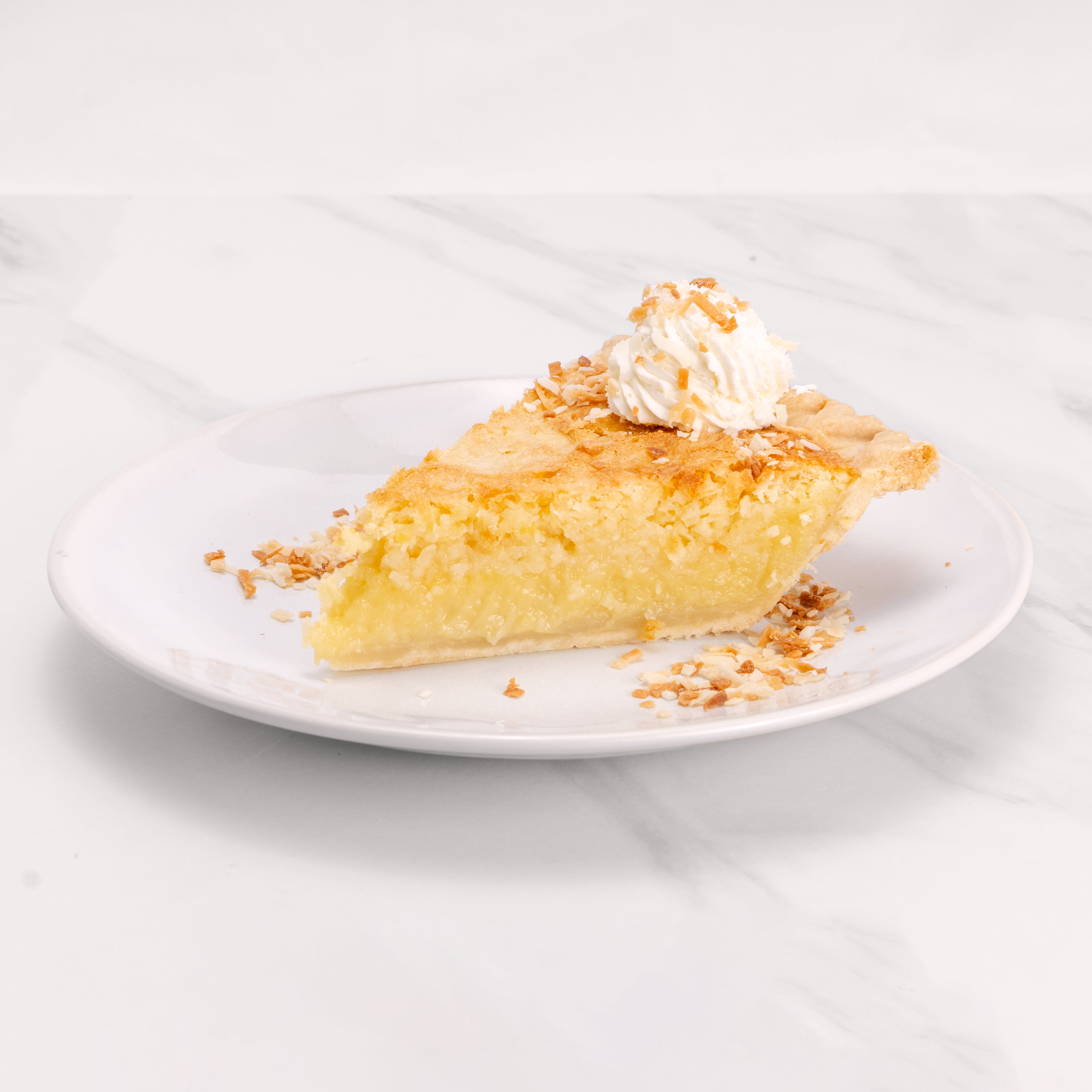 Slice of Coconut Supreme pie garnished with a dollop of crème on top and toasted coconut flakes.