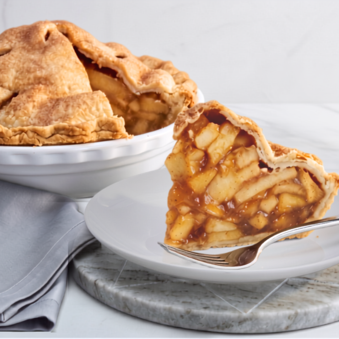 Huge apple pie slice on white plate with fork. Huge apple pie in white dish in the background with a slice cut out. 
