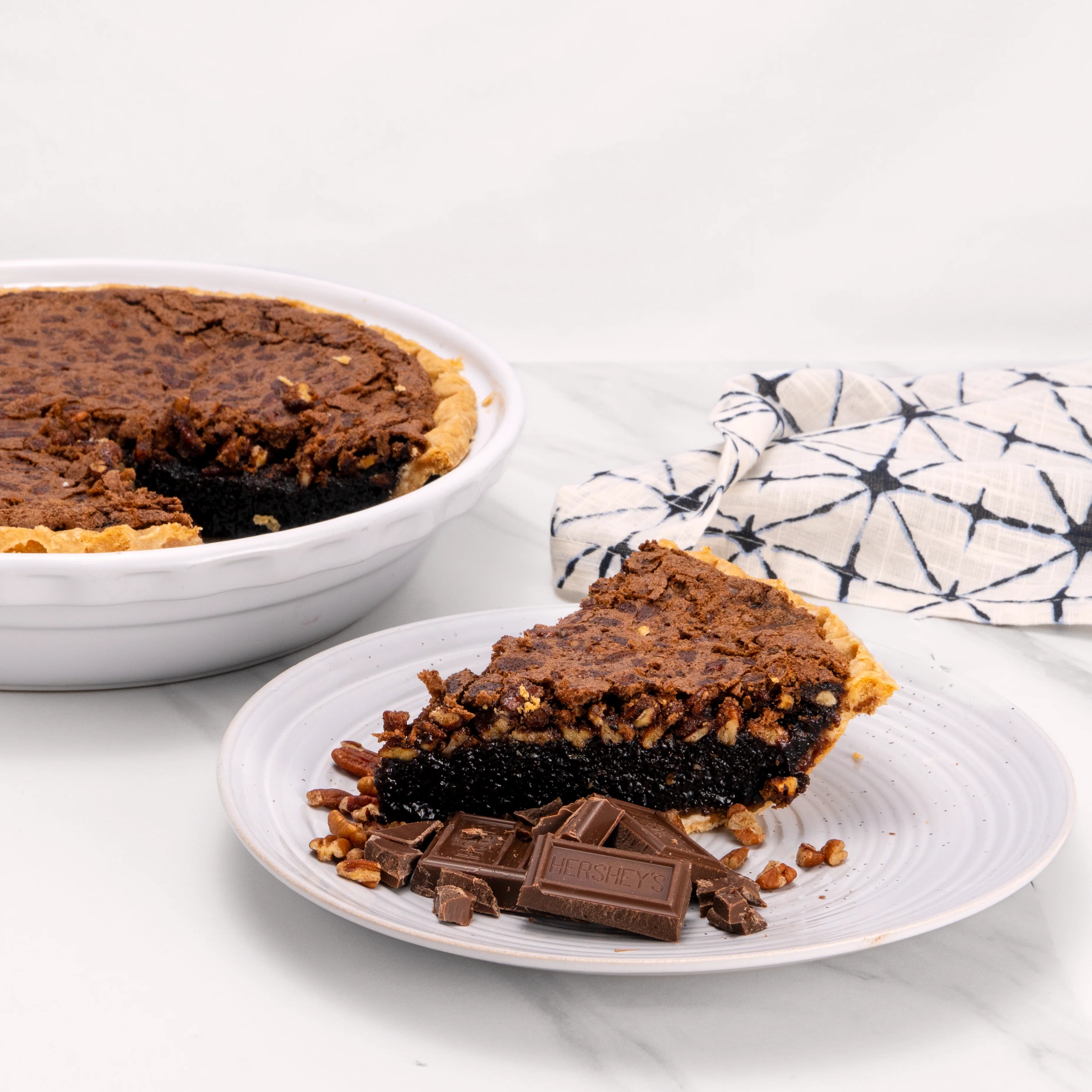 Slice of Chocolate Pecan pie, garnished with chocolate and pecans, in front of an 11" pie from which it was cut.