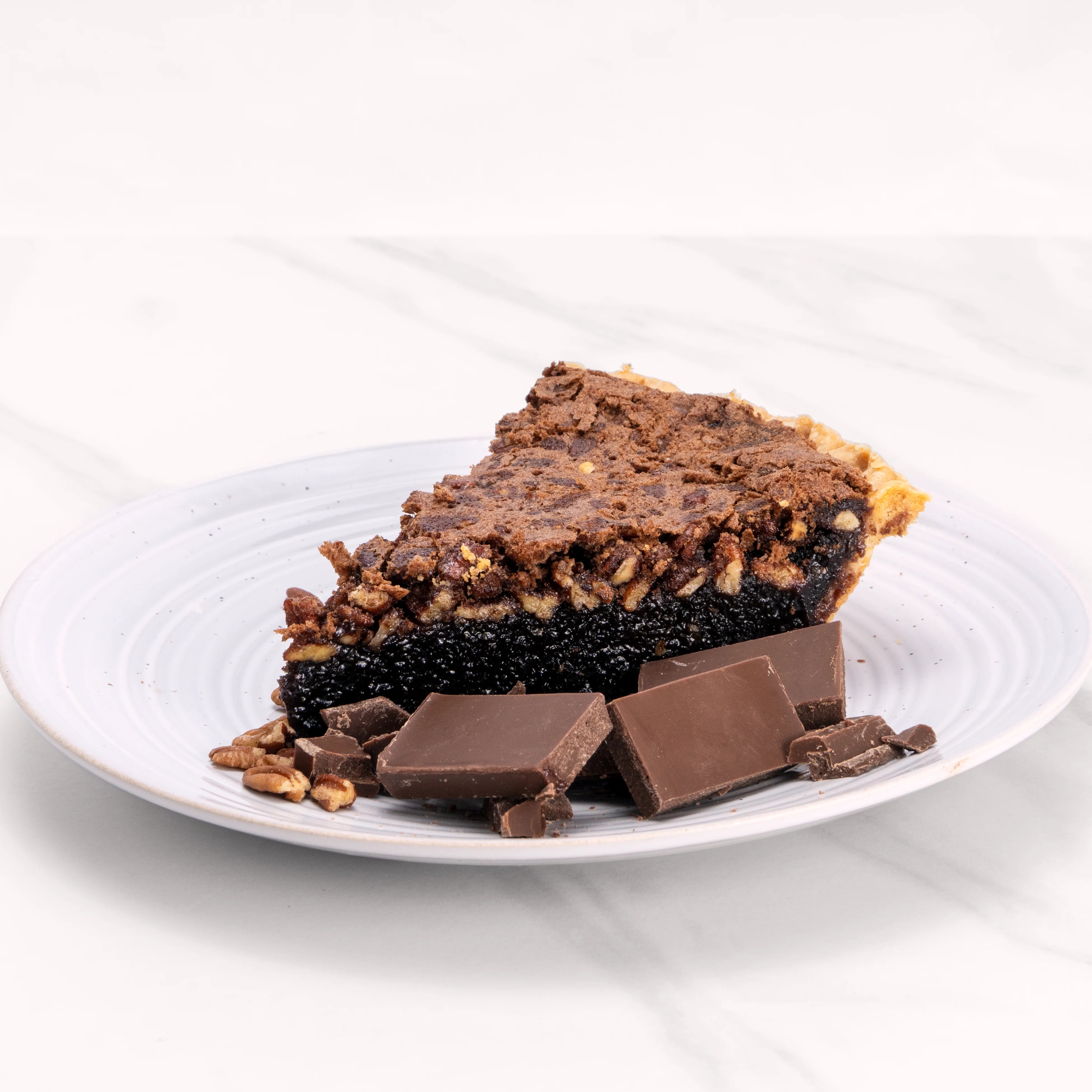 Slice of Chocolate Pecan pie garnished with chocolate and pecans. 