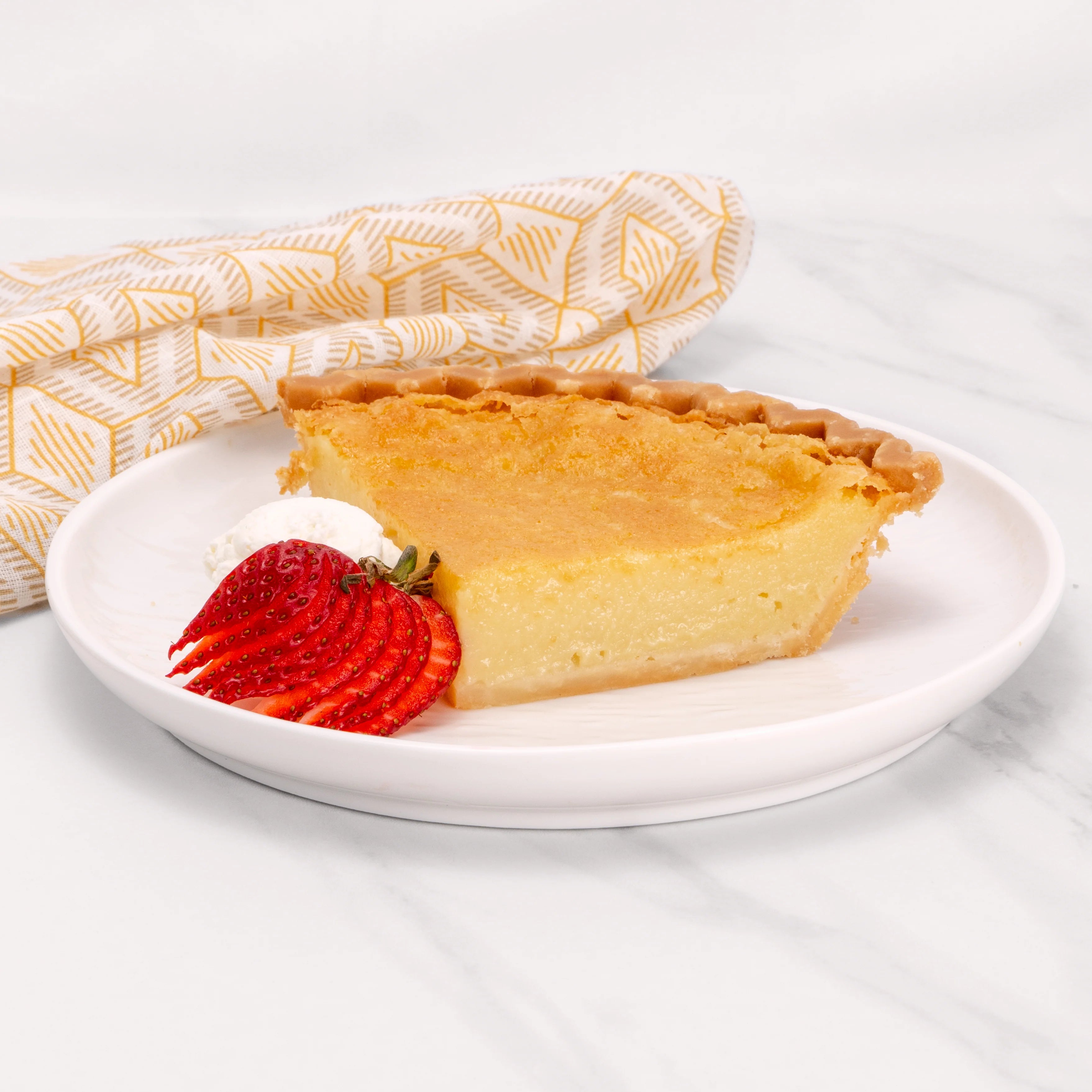 A slice of Gluten Free Buttermilk pie garnished with sliced strawberries and crème.