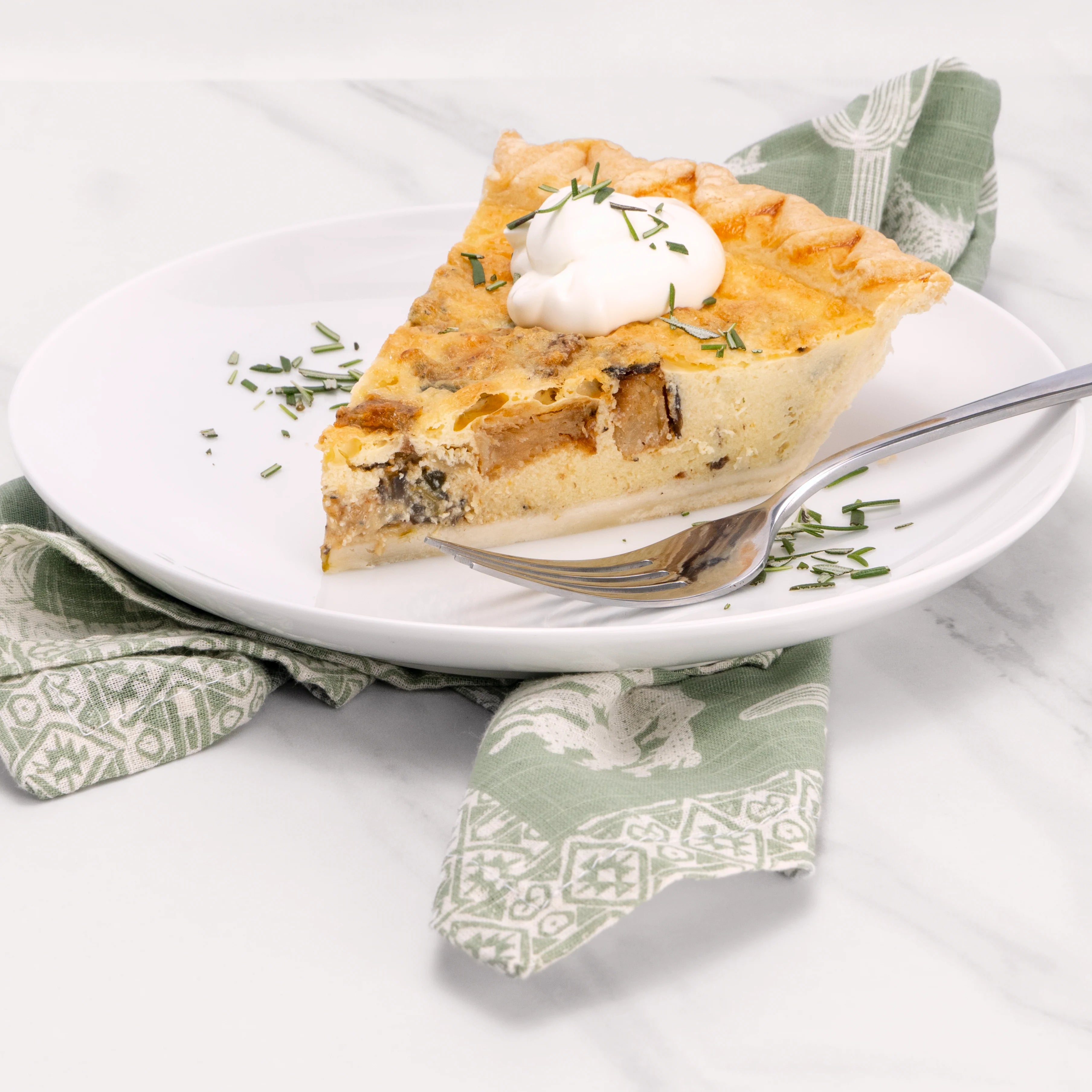 Slice of Hatch Mushroom quiche garnished with rosemary and sour cream.