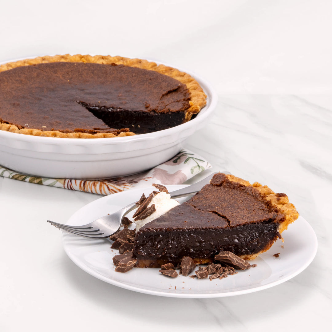 Slice of Heavenly Chocolate Pie, garnished with chocolate and a dollop of crème, in front of an 11" pie from which it was cut.
