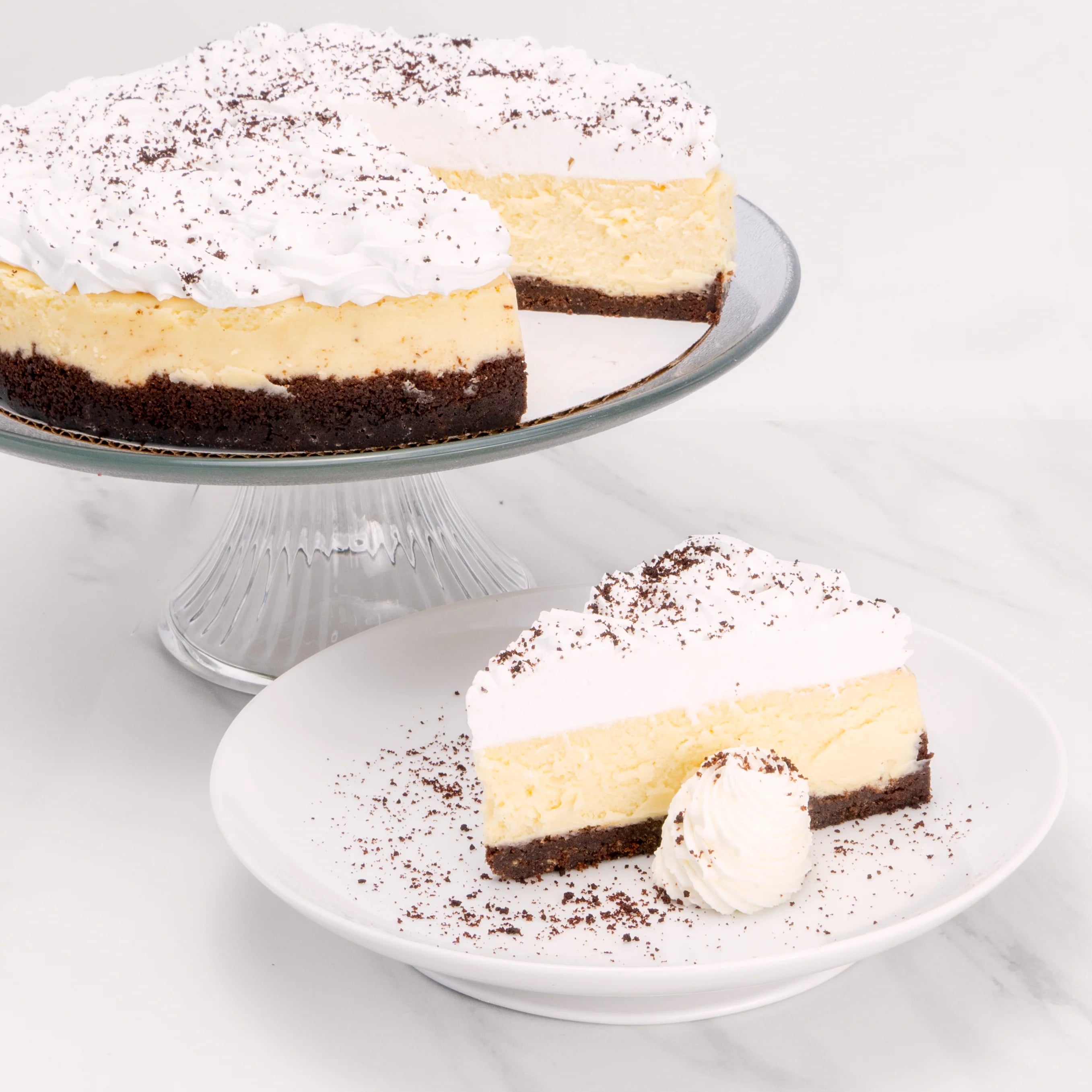 Slice of Irish Whiskey Cheesecake, garnished with chocolate powder and a dollop of crème, in front of a 9" cake from which it was cut.