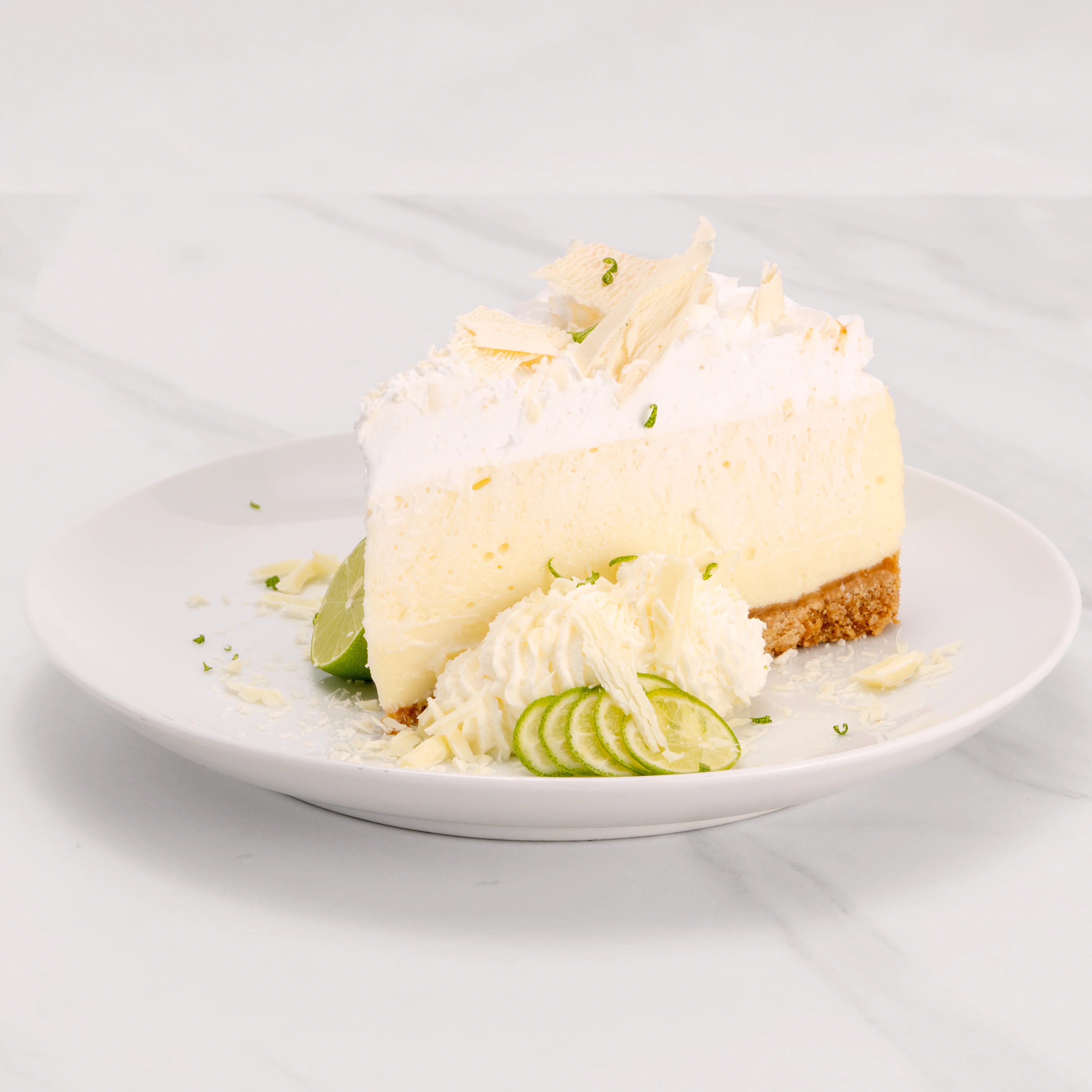 Slice of Gluten Free Key Lime White Chocolate Crème Cake garnished with lime, white chocolate, and a dollop of crème.