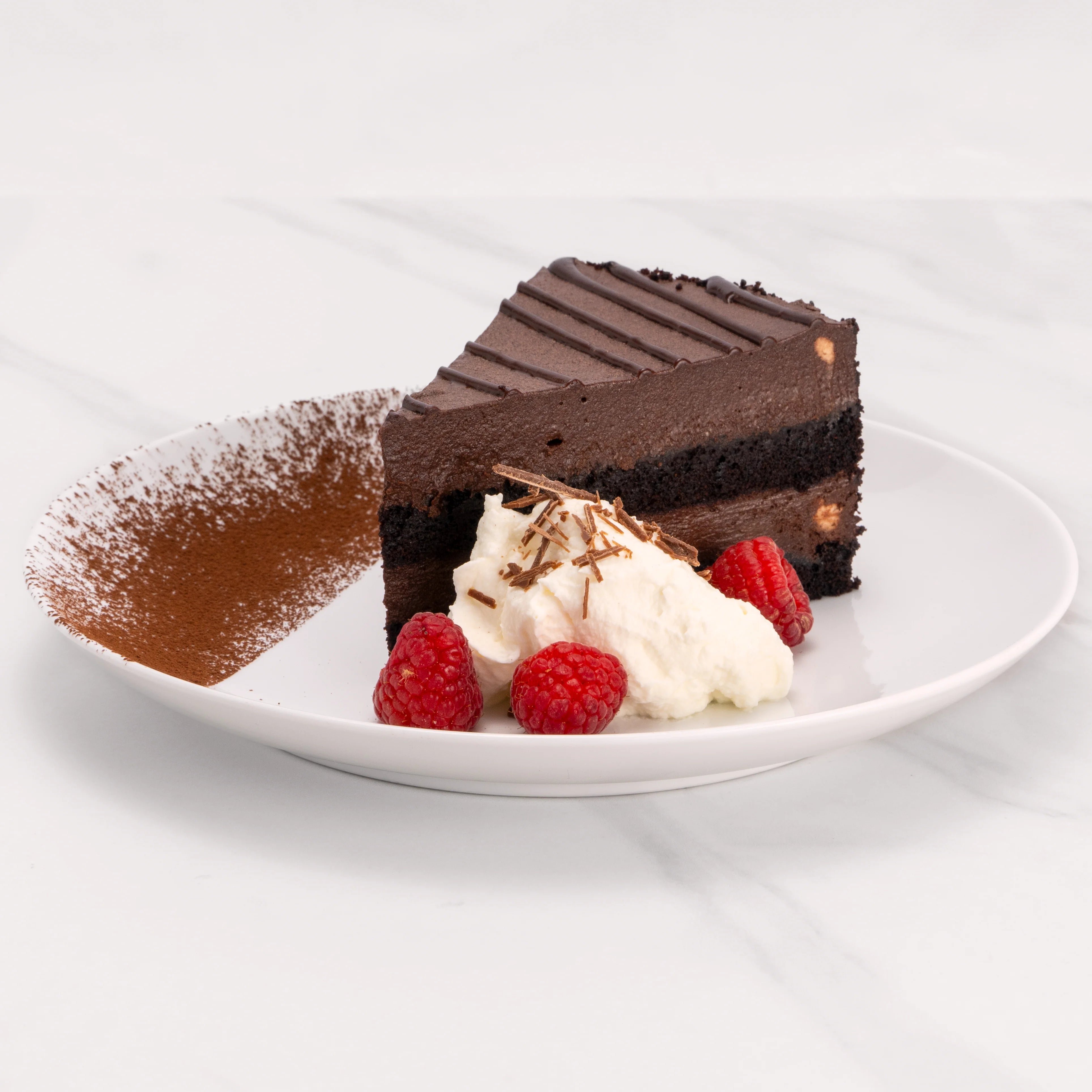 Slice of Gluten Free Chocolate Midnight Marquise Cake garnished with chocolate, raspberries, and a dollop of crème.