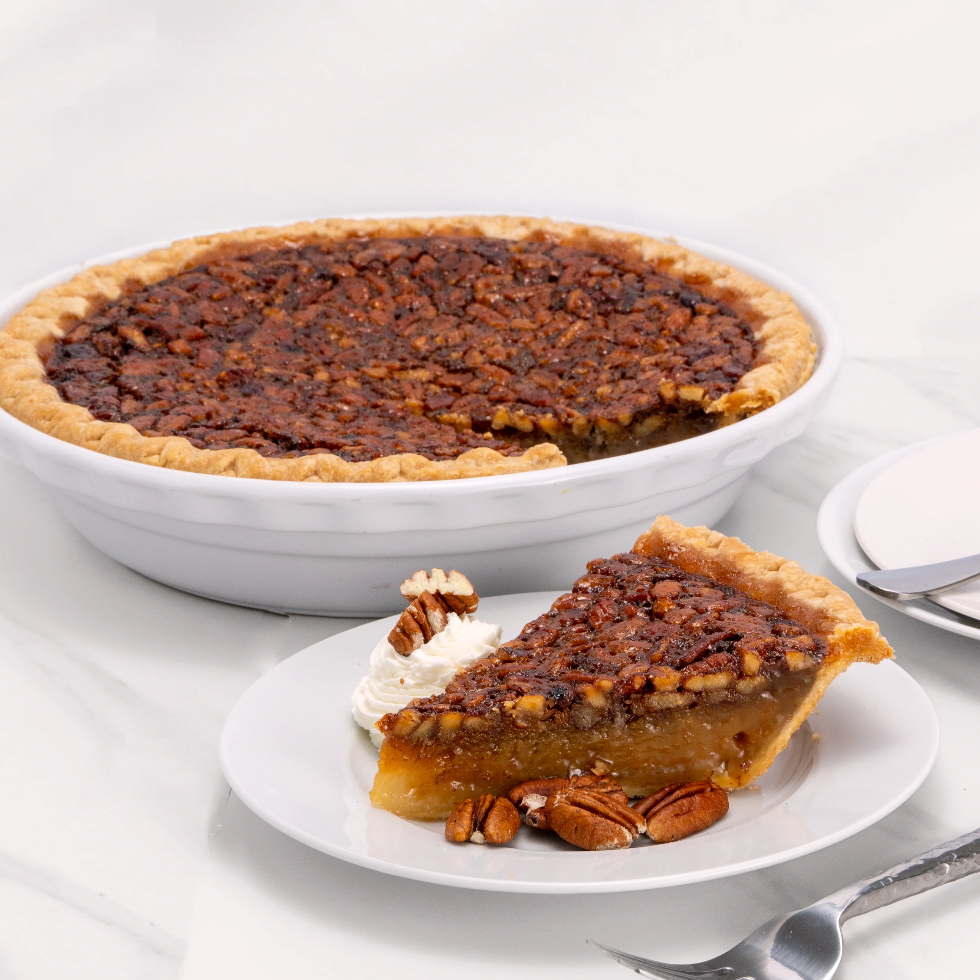 Slice of Pecan Pie, garnished with pecans and crème, in front of an 11" pie from which it was cut.