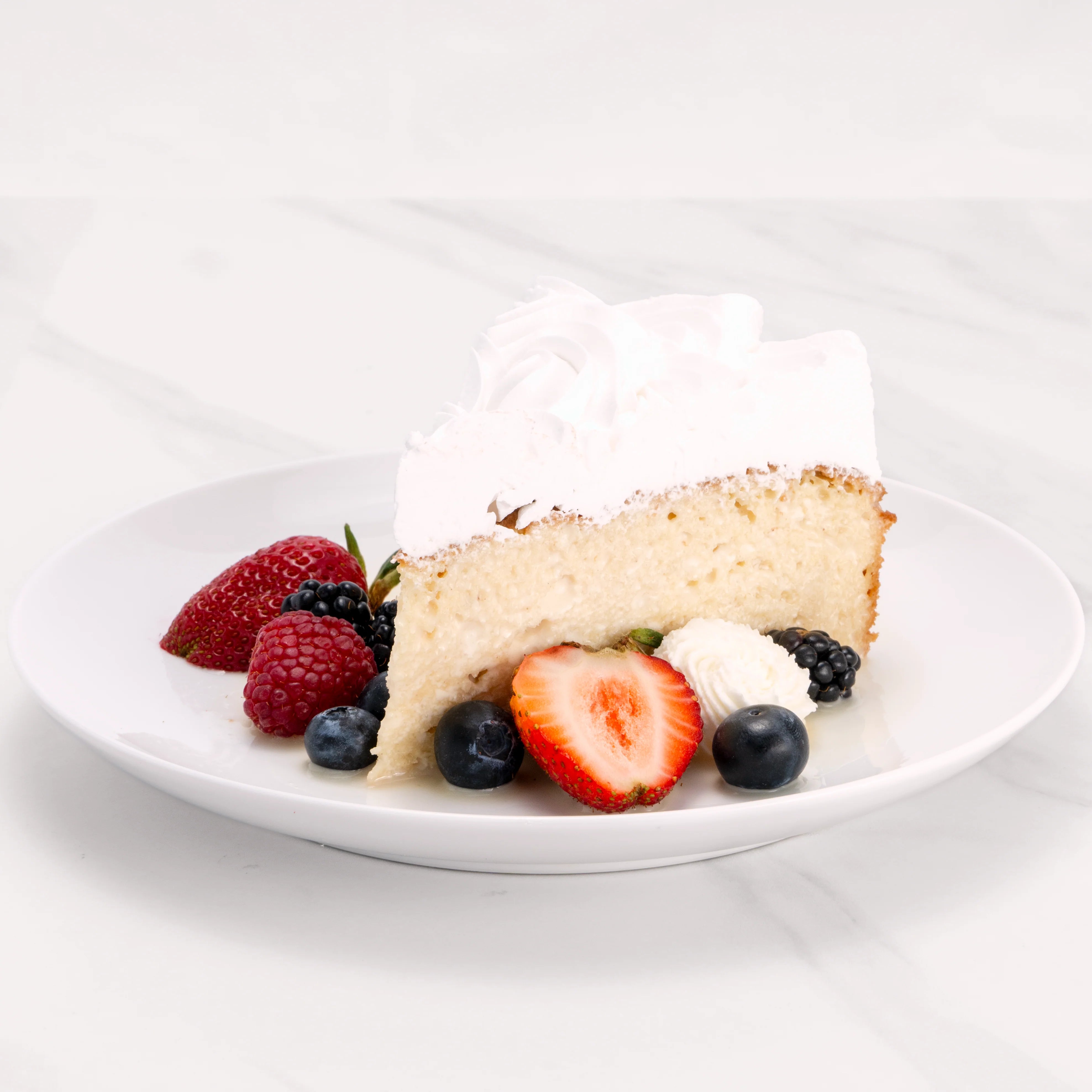 Slice of Tres Leches Cake garnished with blueberries, strawberries, blackberries, and crème.