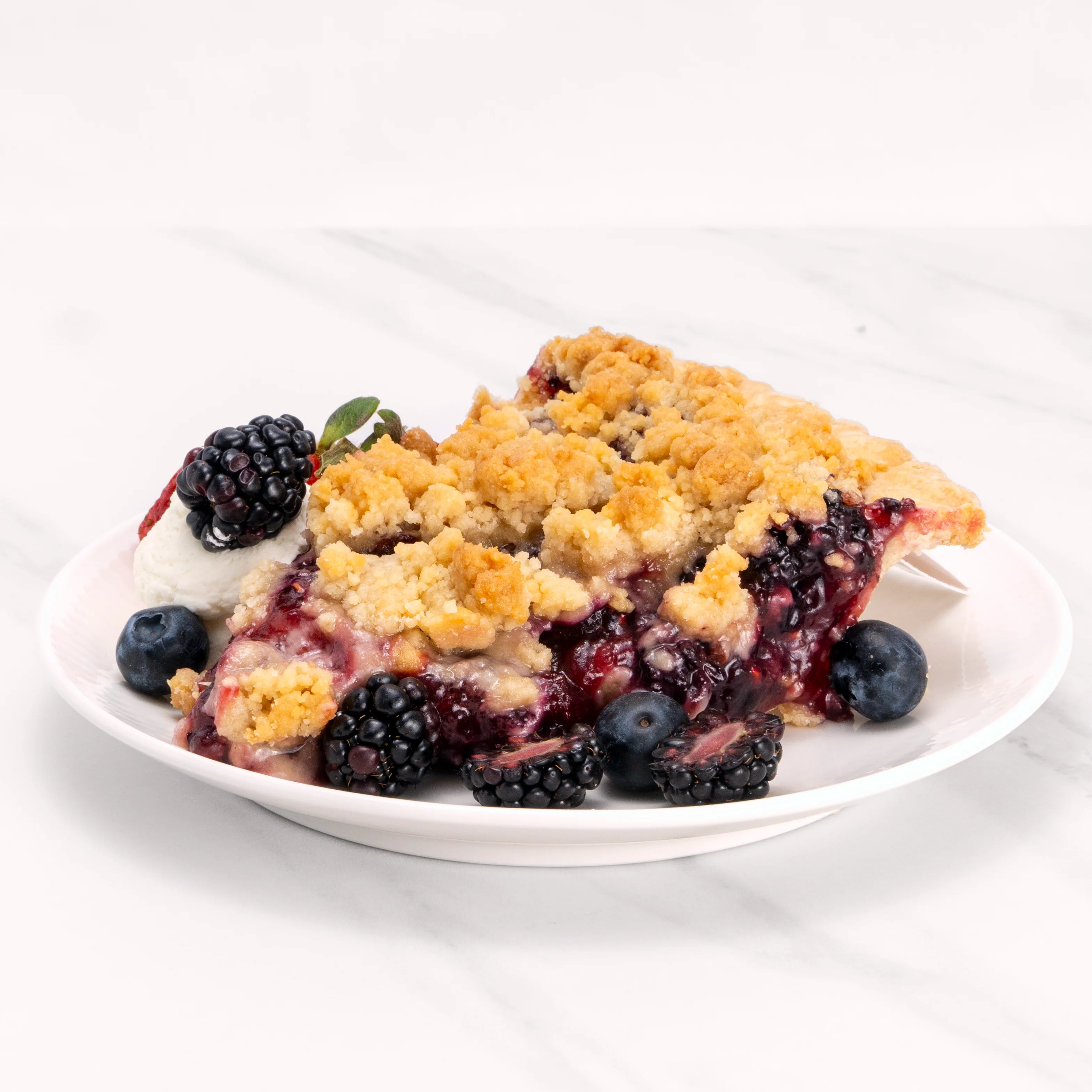 Slice of Triple Berry Pie garnished with blueberries, strawberries, blackberries, and crème.
