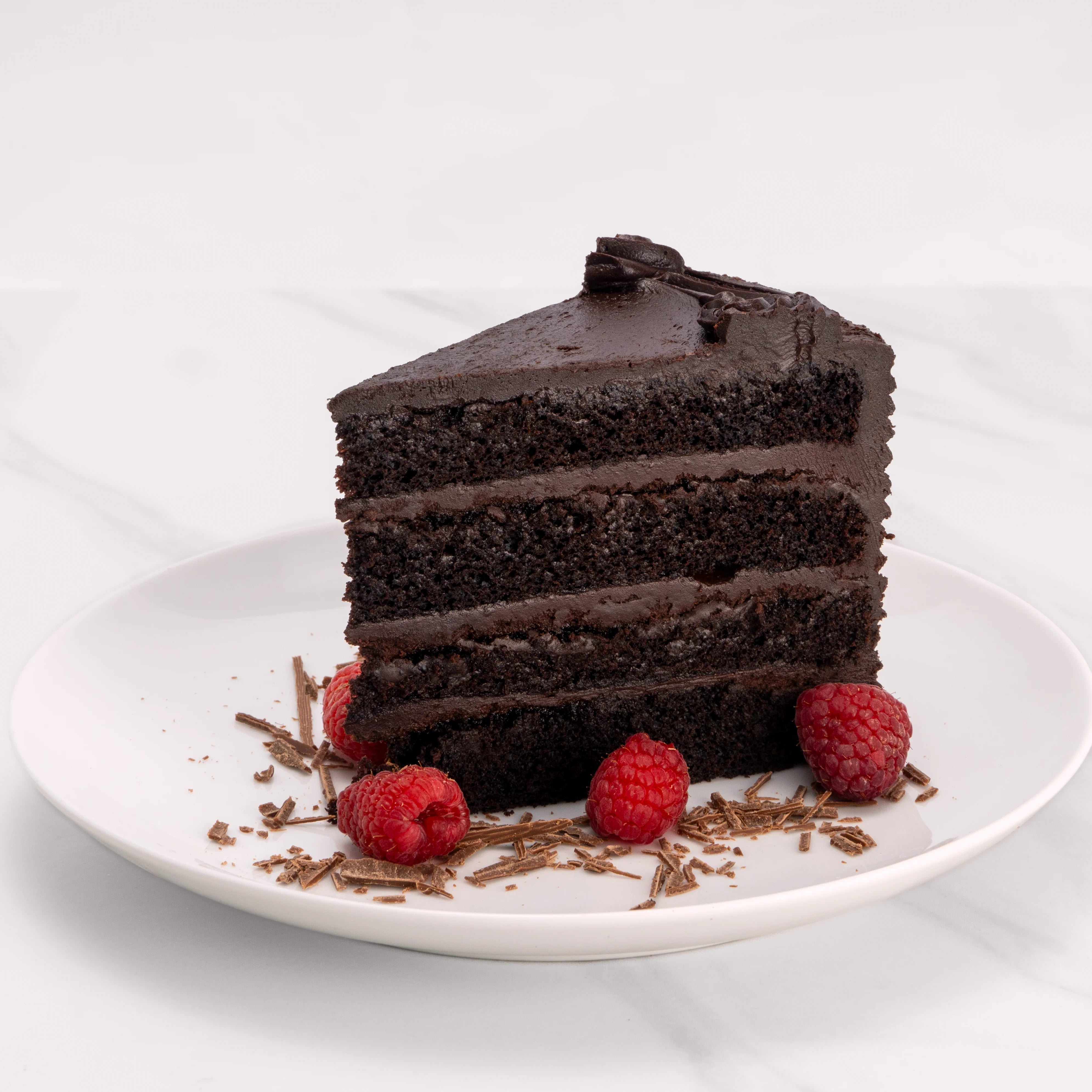 Slice of Heavenly Chocolate Cake garnished with raspberries and chocolate.